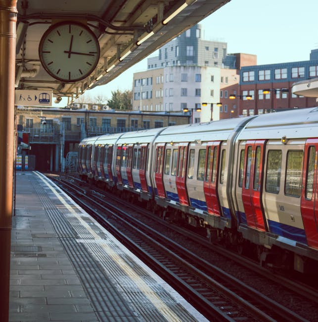 A view of Finsbury Park train station platform showing clean, tiled surfaces with polished metal benches and blue-and-white striped pillars supporting a beige, corrugated roof. The platform appears well-maintained, free of dust or litter, and is illuminated by natural daylight. In the background, visible signs indicate directions and station amenities, with a few passengers seated on benches or walking along the platform. The overall scene emphasizes the clean, hygienic environment typical of professional station maintenance, reflecting the quality service offered by Cleaners N4 for domestic and commercial cleaning, including surface cleaning and sanitisation tasks.